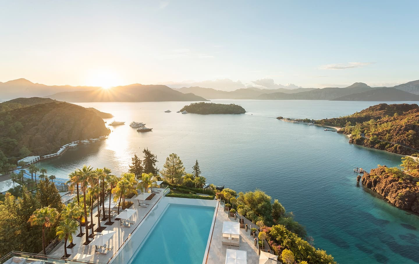 A panoramic bay view over the pool, palms and yachts at D Maris Bay at sunrise