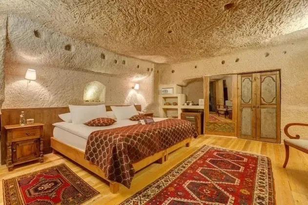 A cave room at Taşkonaklar with a carved stone ceiling, a carved wooden bed and kilim rugs