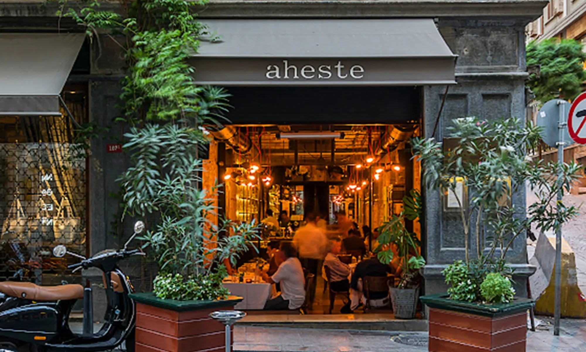 The warmly lit entrance of Aheste in Pera, with an open dining room behind ivy and potted plants