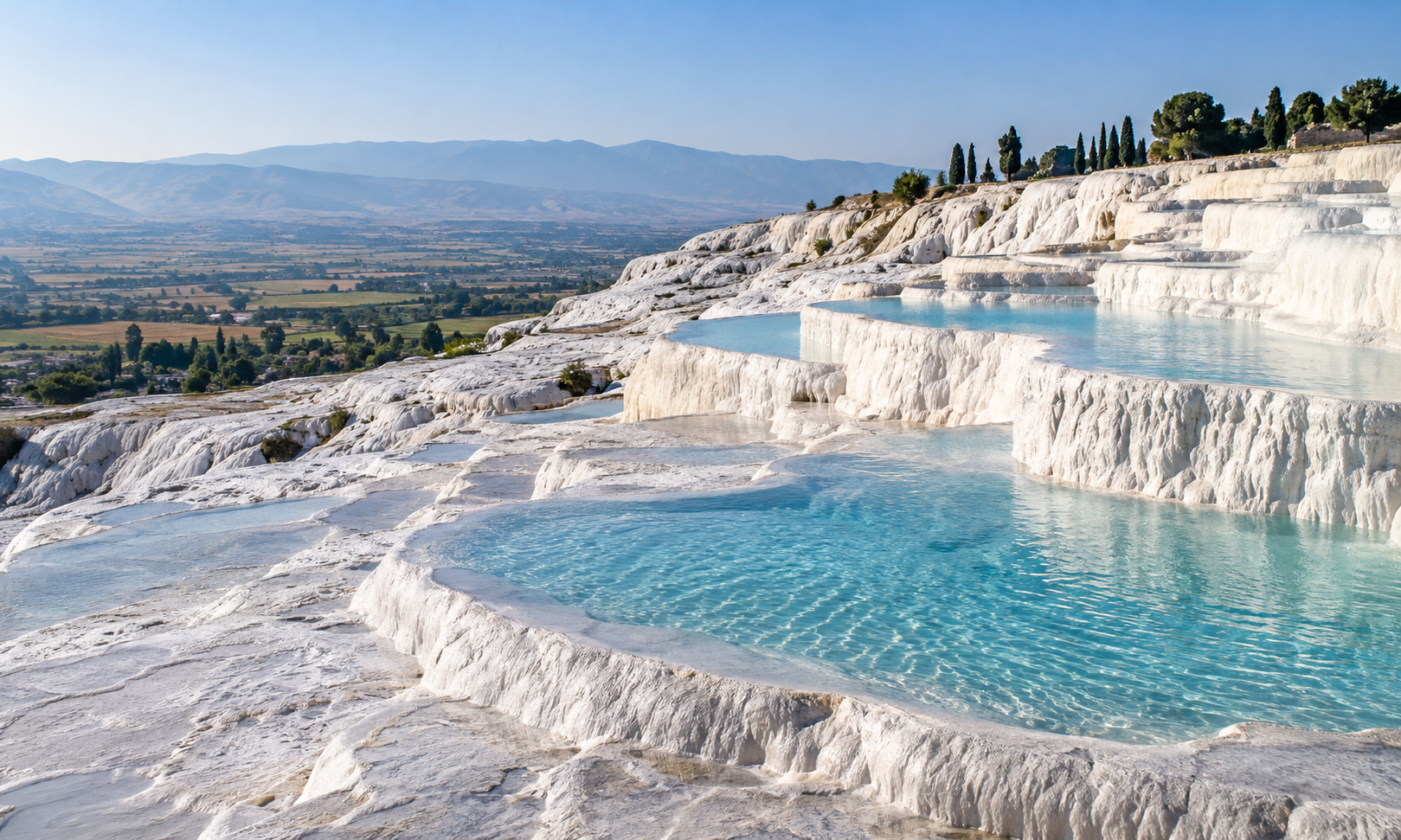 White travertine terraces holding pools of pale blue water above a wide valley