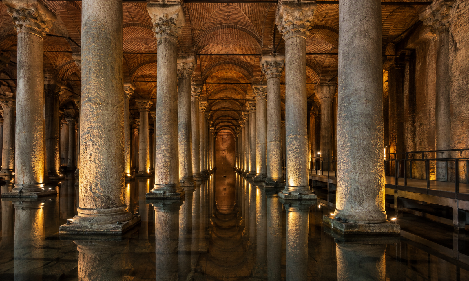 Rows of lit marble columns rising from still water beneath brick vaults in an underground cistern