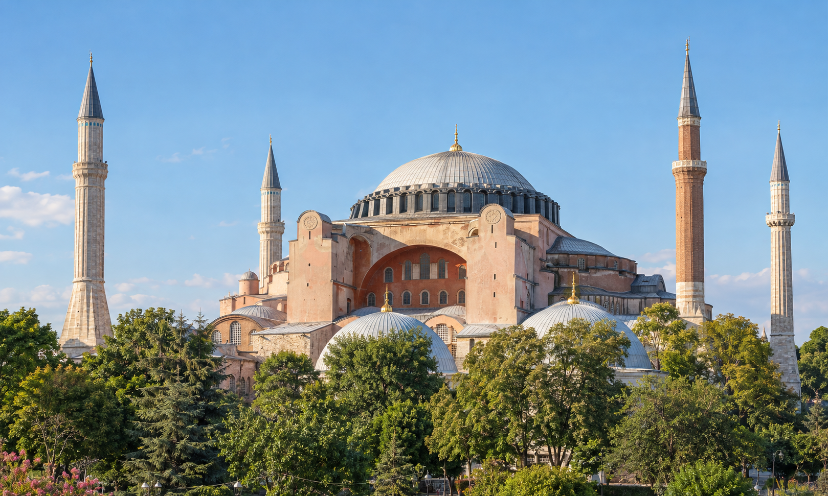 The domed exterior of a great Byzantine-era building with four minarets above green trees