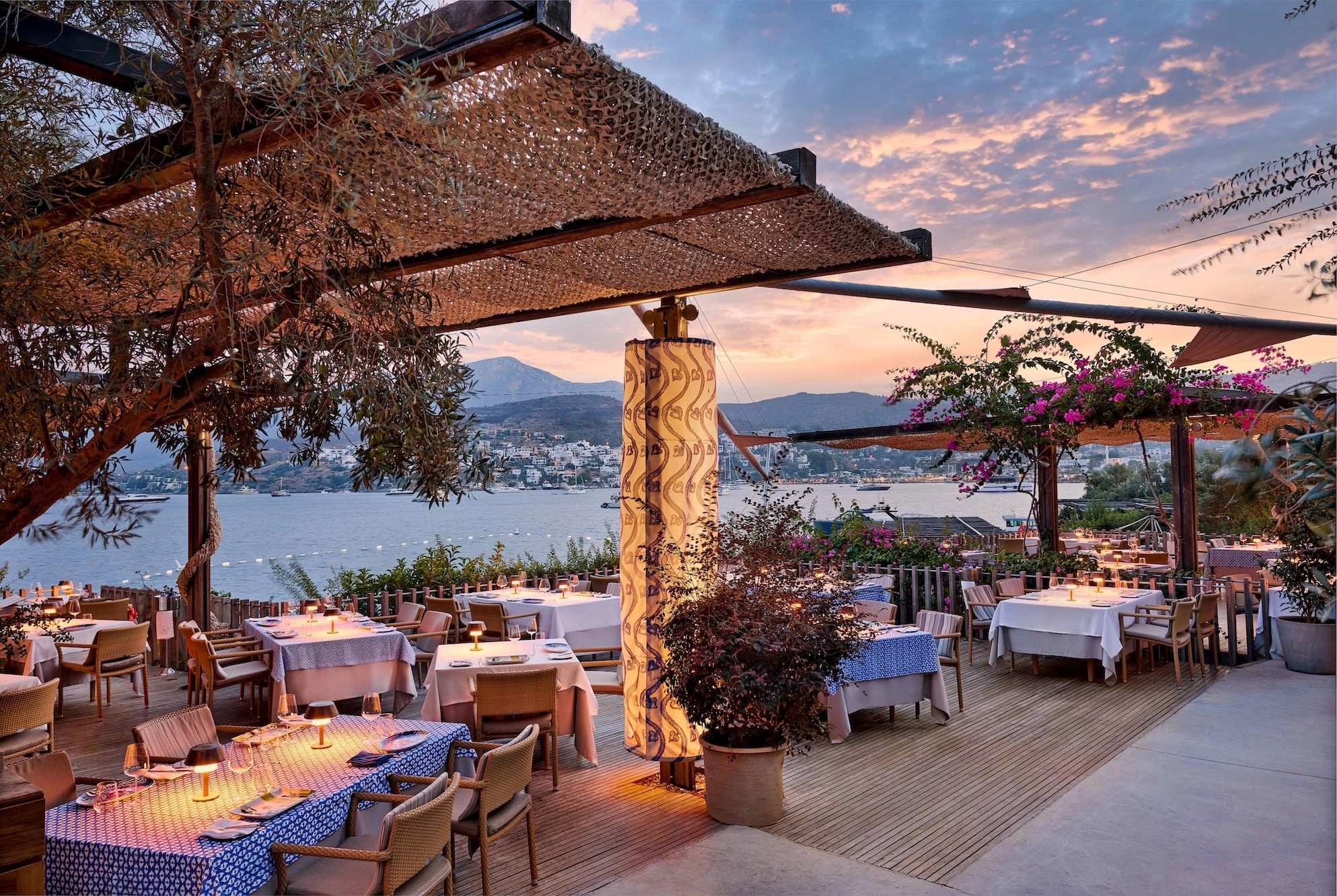 Maçakızı's terrace restaurant with set tables under a pergola at sunset above the bay