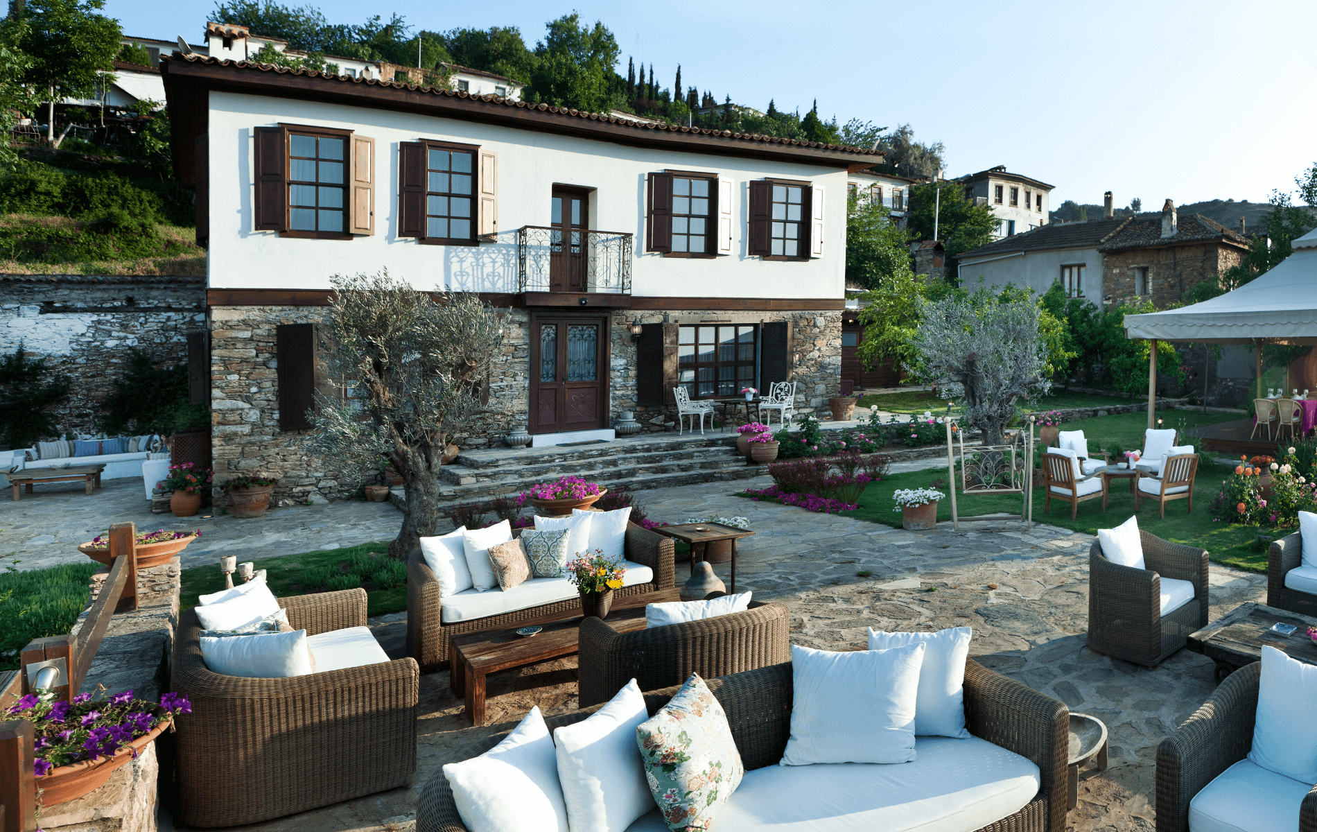 A whitewashed stone mansion of Güllü Konakları above a garden terrace with cushioned seating