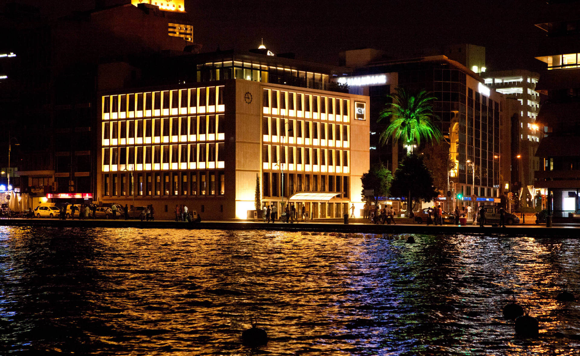 The lit façade of Key Hotel reflected in the water of the İzmir waterfront at night