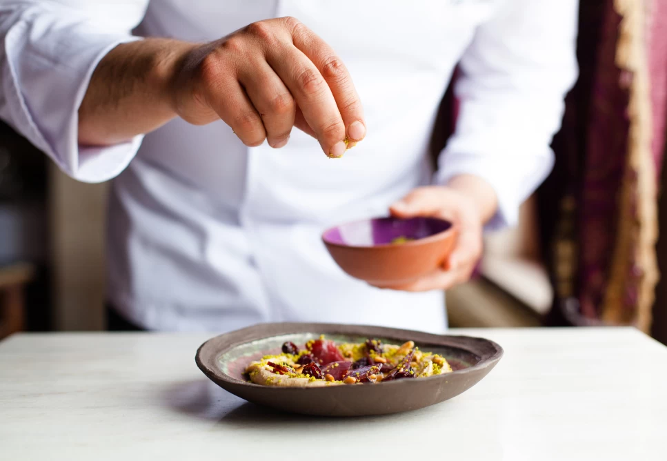 A chef finishing a plated dish at Lil'a Restaurant, Museum Hotel