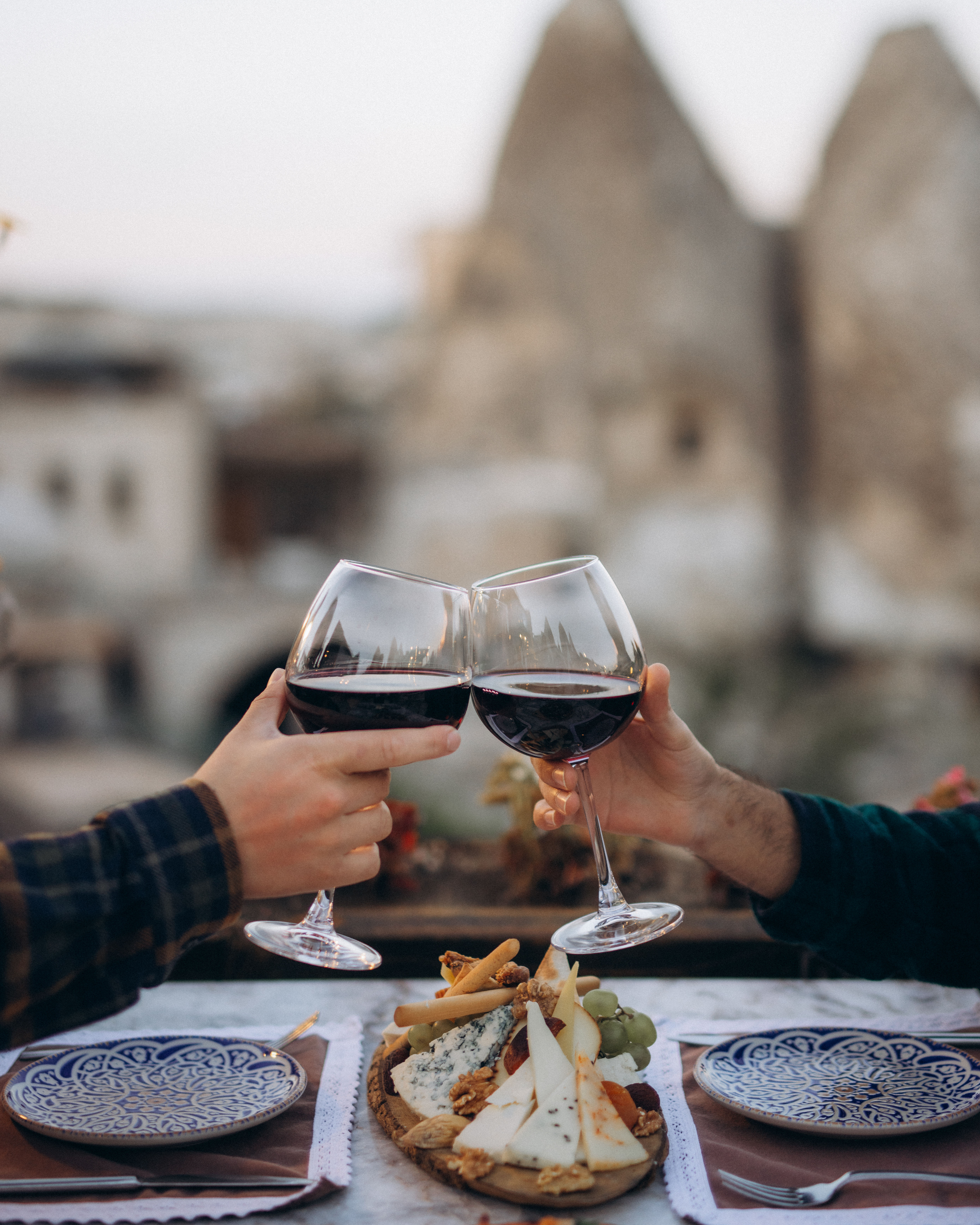 Two glasses of red wine raised over a table at Seten Restaurant, with fairy chimneys behind