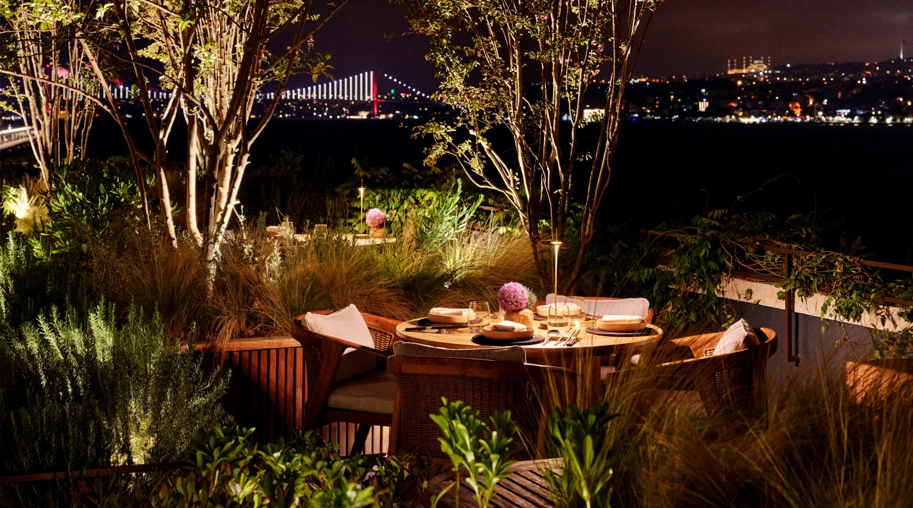 A candlelit table on GALLADA's garden terrace at night, with the lit Bosphorus bridge beyond